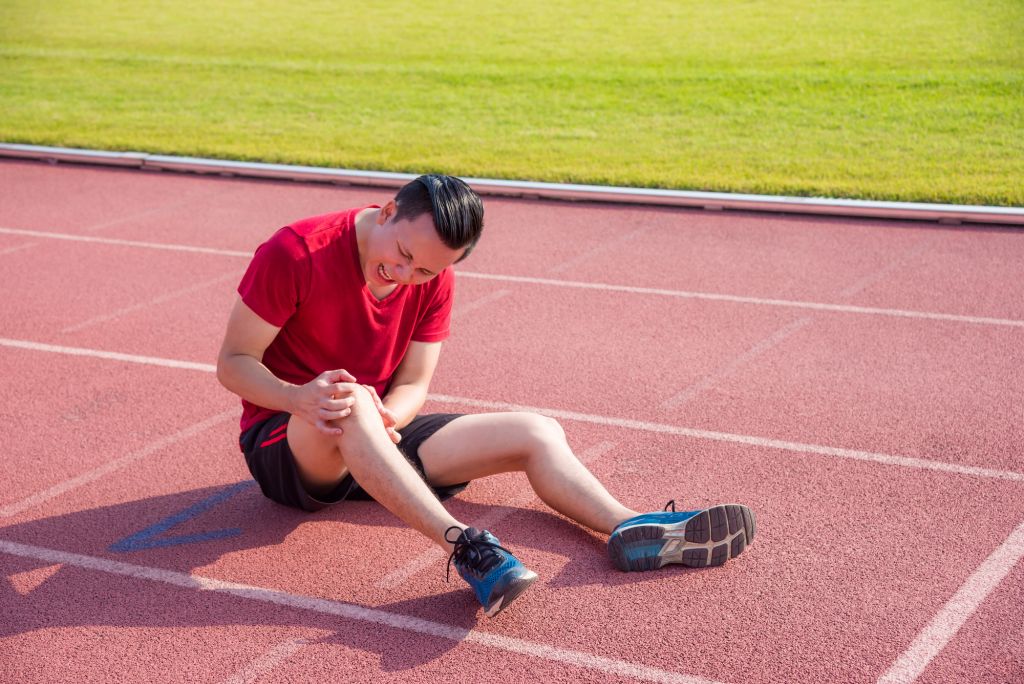 Young asian runner having pain at knee between running in stadiu